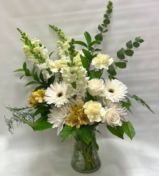 a white green and yellow floral arrangement in a glass cylinder vase