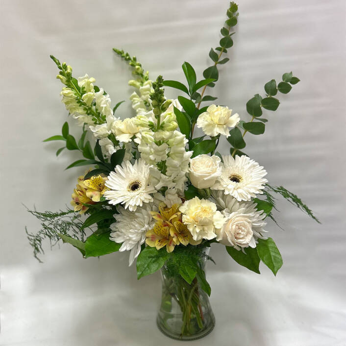 a white green and yellow floral arrangement in a glass cylinder vase