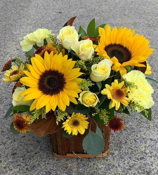 a yellow and brown floral arrangement in a brown wooden box. The arrangement is filled with sunflowers and yellow roses.