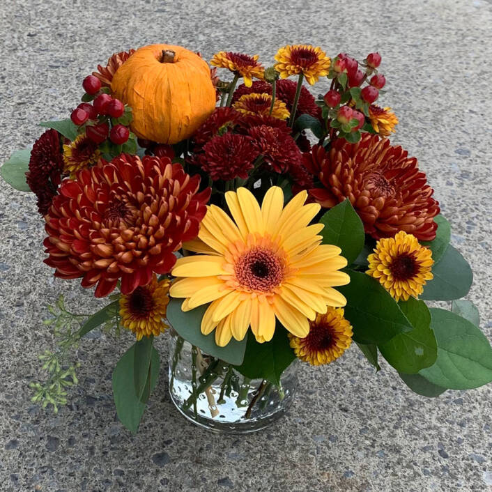 a fall yellow orange and red floral arrangement in a small glass cylinder vase.