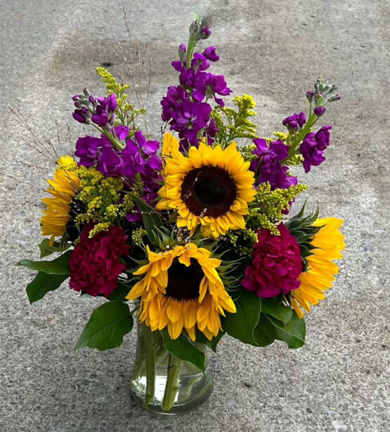 a yellow and purple fall floral arrangement with sunflowers in a glass vase