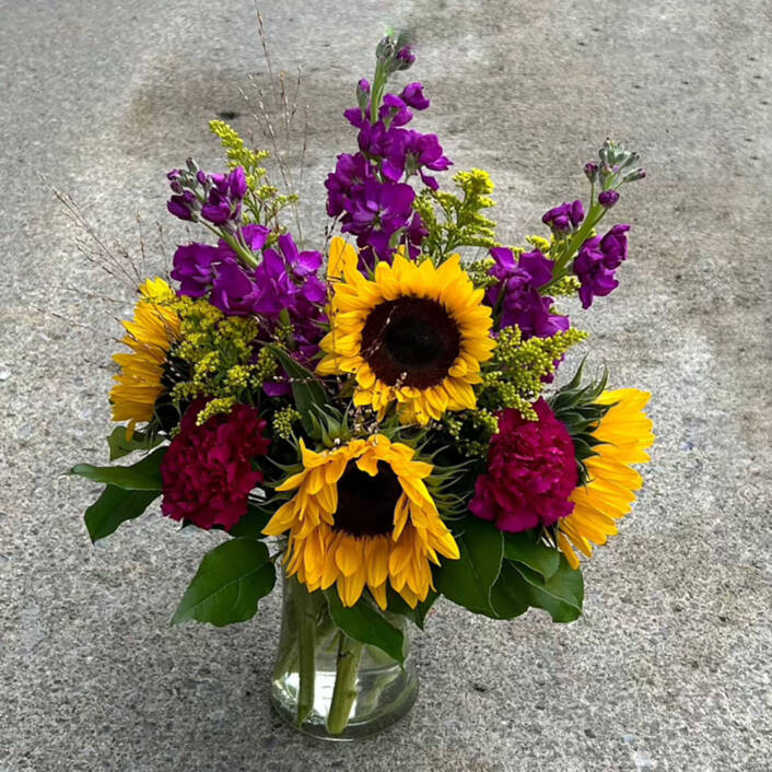 a yellow and purple fall floral arrangement with sunflowers in a glass vase