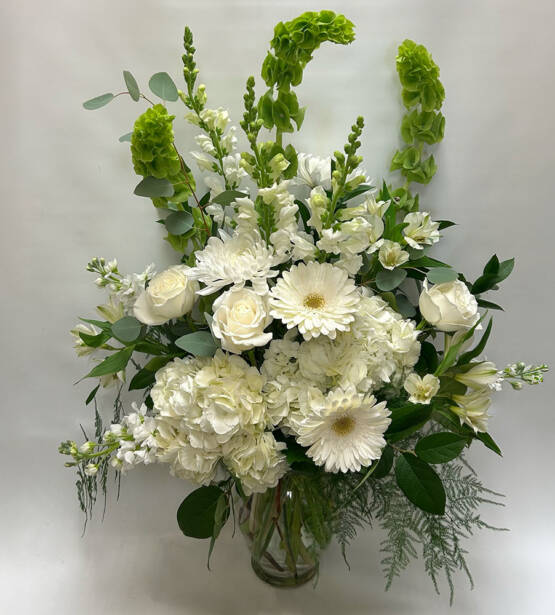 a tall white floral arrangement in a glass vase