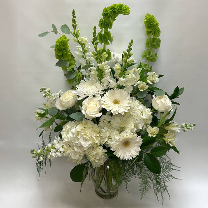 a tall white floral arrangement in a glass vase