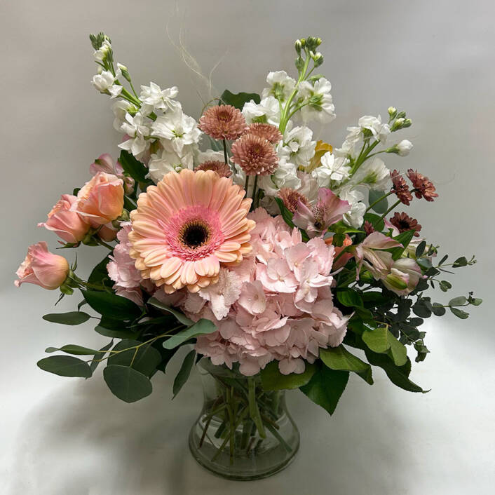 a pink and white floral arrangement in a glass vase